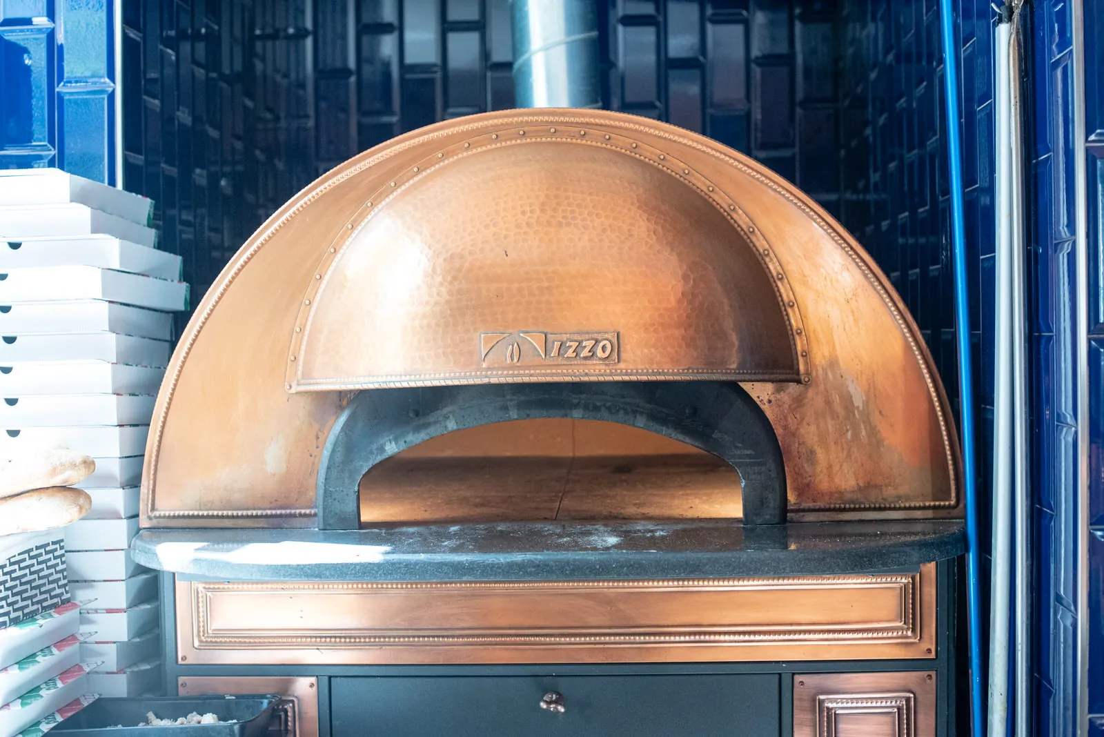 El horno de cobre de Via Napoli, de frente, con la boca abierta y cajas de pizza apiladas a un lado