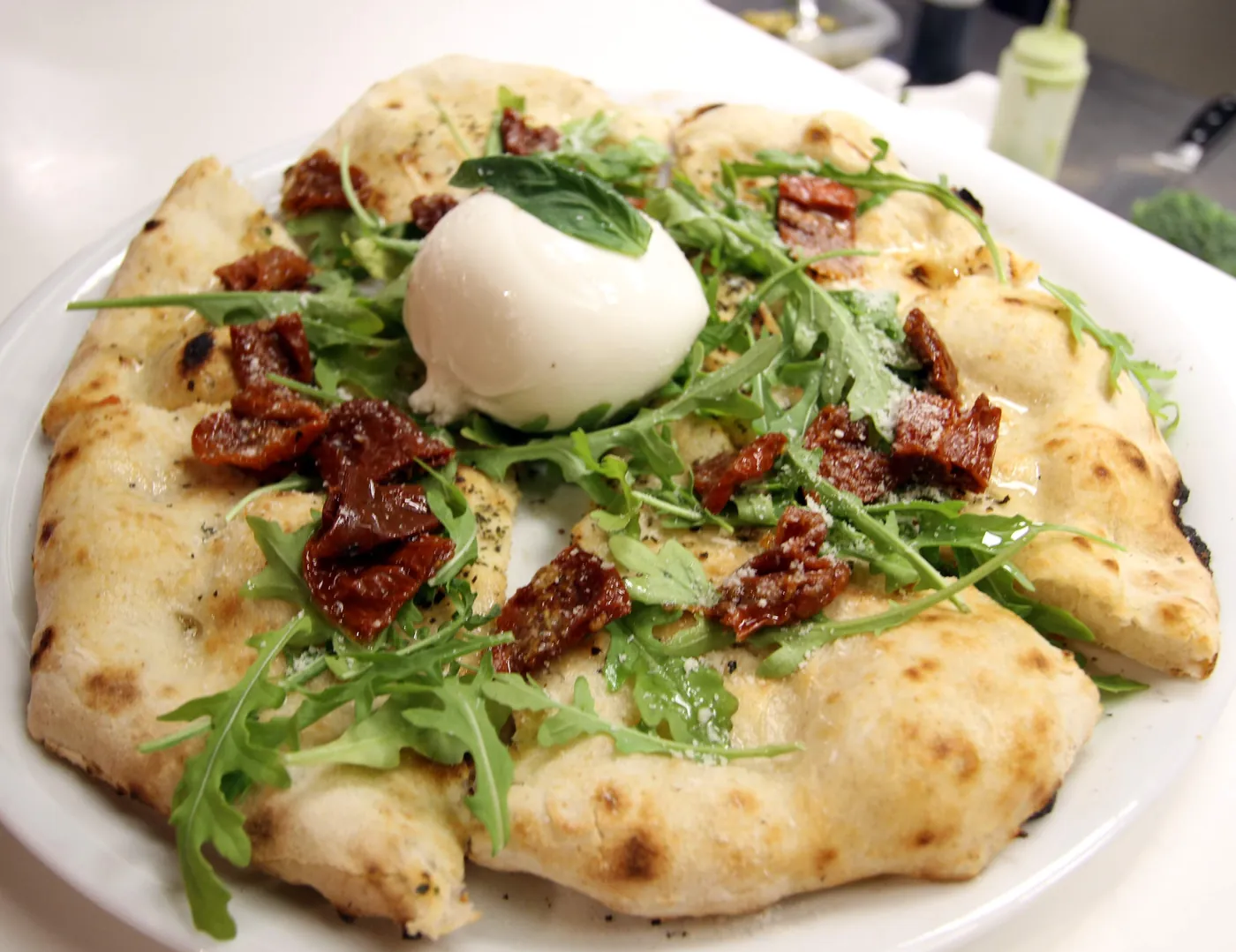 Pizza blanca con una burrata entera en el centro, rúcula y tomate semiseco