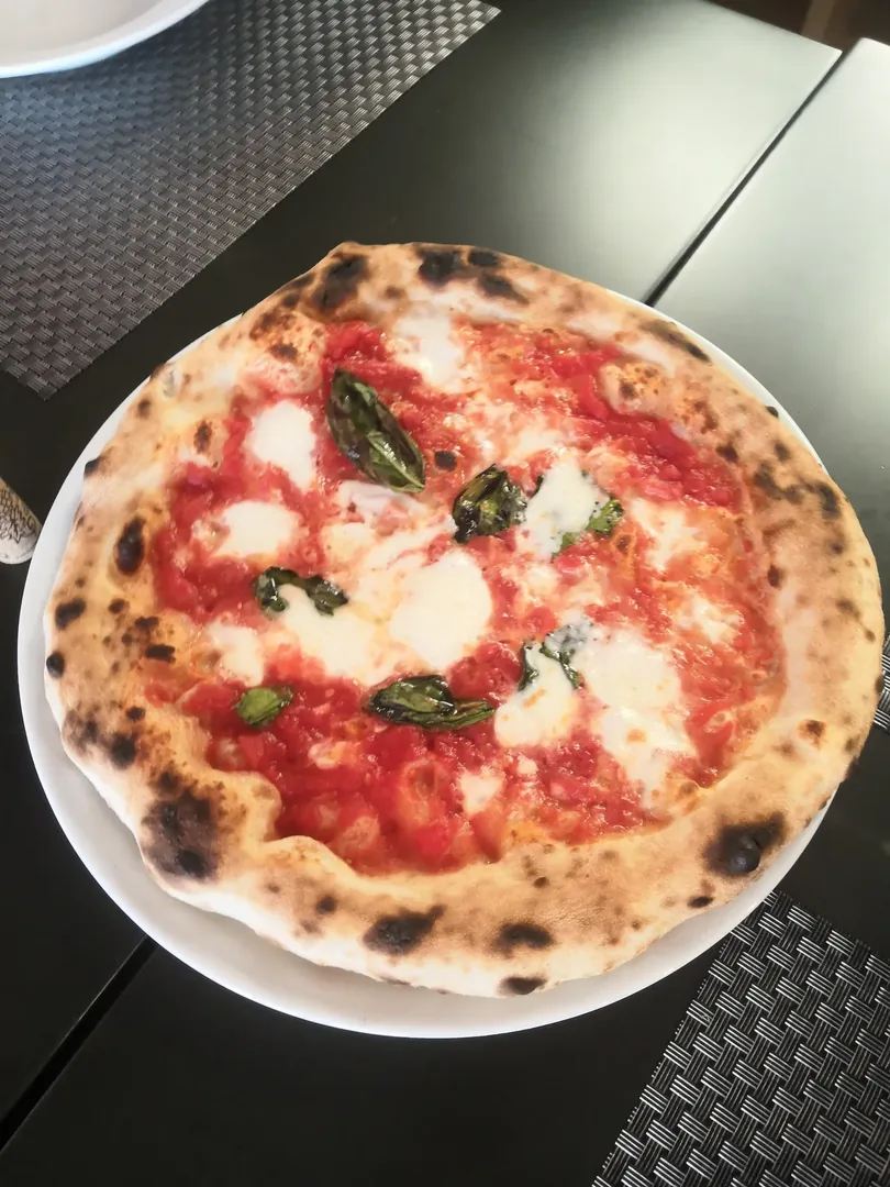 Una pizza margherita entera sobre la mesa, con el borde tostado y hojas de albahaca