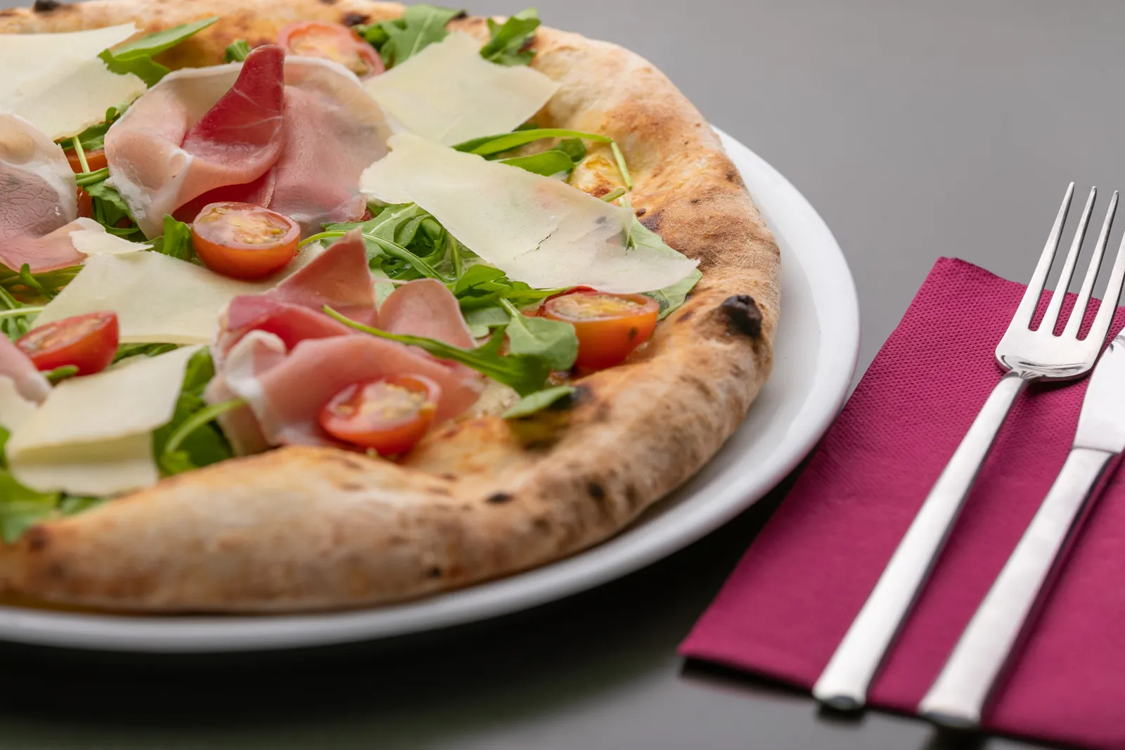 Pizza con jamón crudo, rúcula, tomates cherry y lascas de parmesano, con el borde tostado